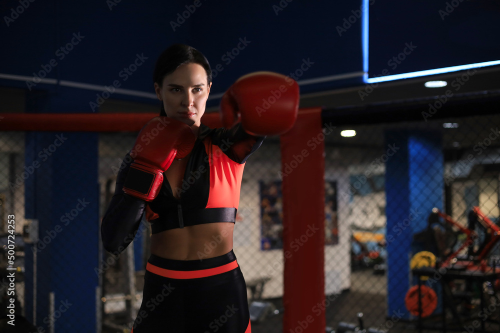 Female in red boxing gloves and sportive wear stands in a rack in the boxing hall.