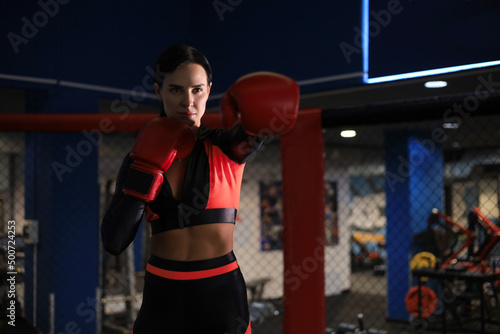 Female in red boxing gloves and sportive wear stands in a rack in the boxing hall.