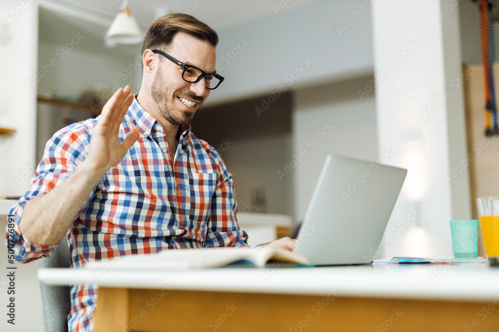 Happy mid adult man waving to someone while having a video call over computer at home Happy mid adult man waving to someone while having a video call over computer at home