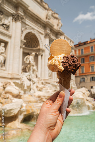 Gelato is Italian ice cream. Ice cream cone in a woman's hand against the backdrop of the Trevi Fountain.