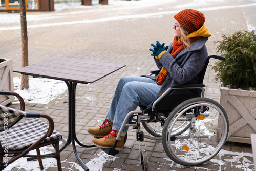 Caucasian woman in wheelchair sitting at outdoor cafe table. 