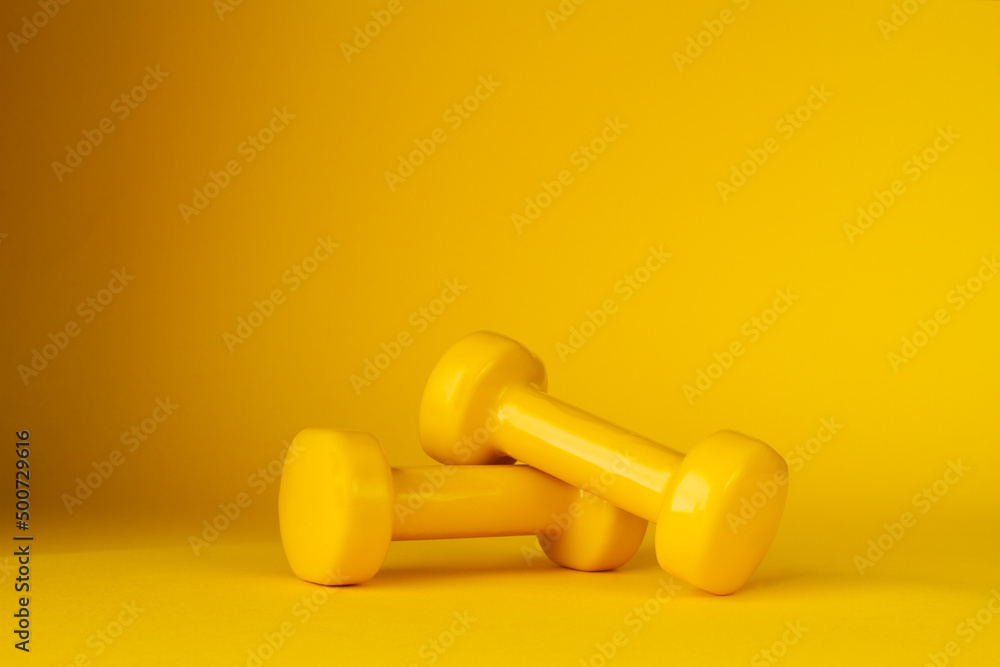 Two heavy dumbbells for workout, with copy space on yellow background. Gym composition, fit exercise at home. Two heavy dumbbells for workout, with copy space on yellow background. Gym composition, fit exercise at home.