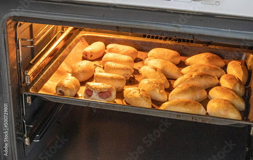 The concept of cooking homemade food, freshly baked hot pies with filling on a baking sheet in the oven