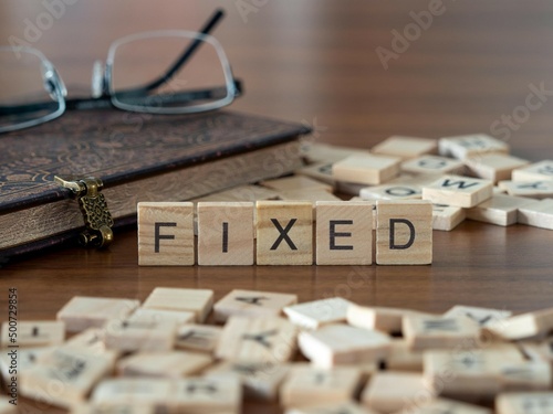 fixed word or concept represented by wooden letter tiles on a wooden table with glasses and a book photo