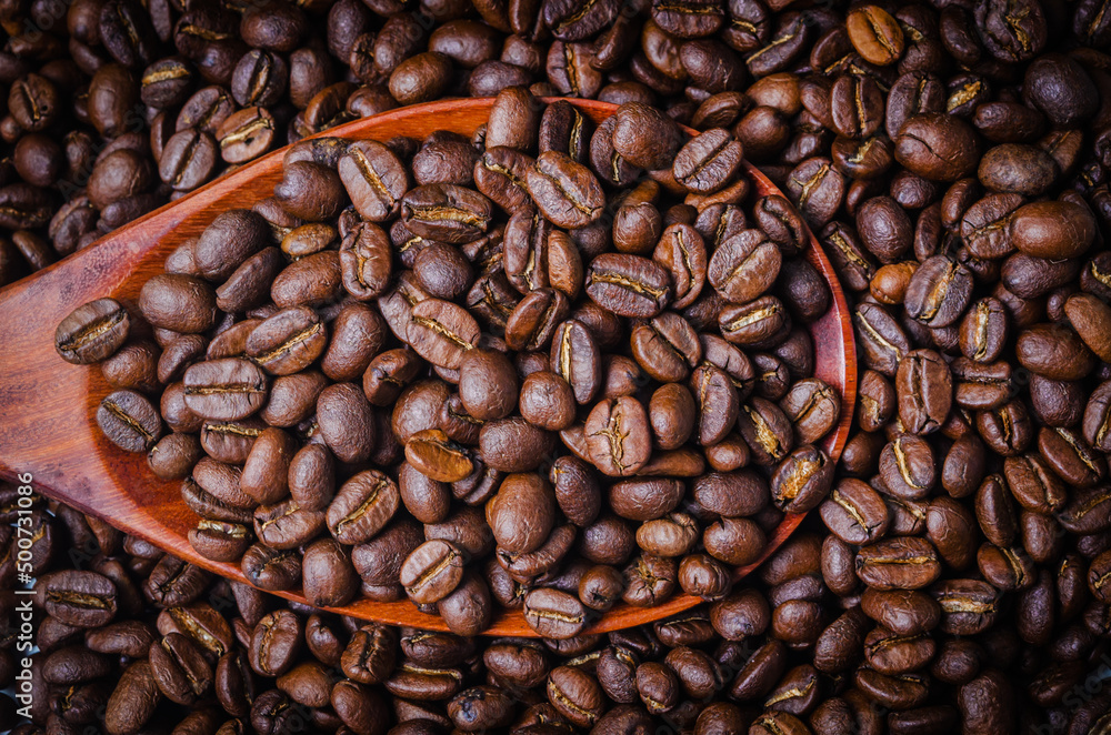 Obraz premium Black coffee beans in a wooden spoon.