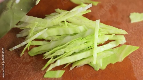 Thinly slicing green cabbage in slow motion macro video.  Bunka style chef knife being used to prepare fresh vegetables for dinner.