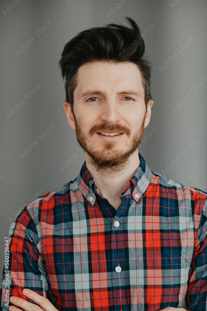 Portraot of Handsome young bearded man in a plaid shirt by a grey background Portraot of Handsome young bearded man in a plaid shirt by a grey background