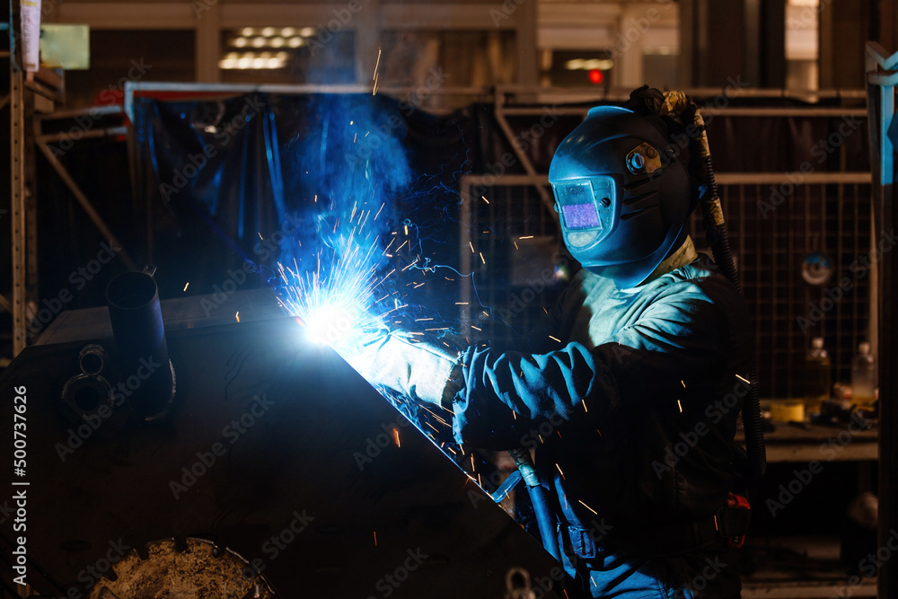 Factory worker in protective mask welding iron parts Factory worker in protective mask welding iron parts