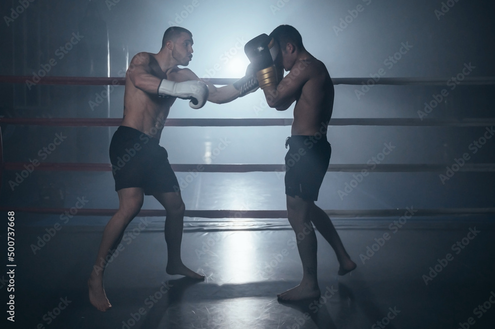 Obraz premium Two shirtless muscular man fighting Kick boxing combat in boxing ring. High quality photo