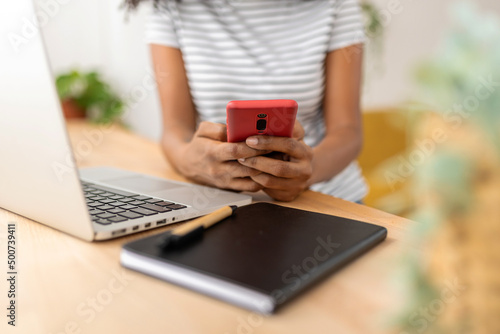 Close-up view of a woman using her mobile phone while working at home. Technology concept.