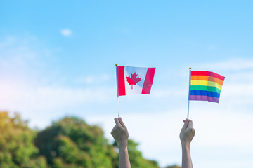 hands showing LGBTQ Rainbow and Canada flag on nature background. Support Lesbian, Gay, Bisexual, Transgender and Queer community and Pride month concept
