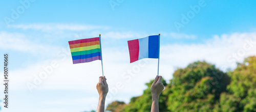 Photography hands showing LGBTQ Rainbow and France flag on nature background