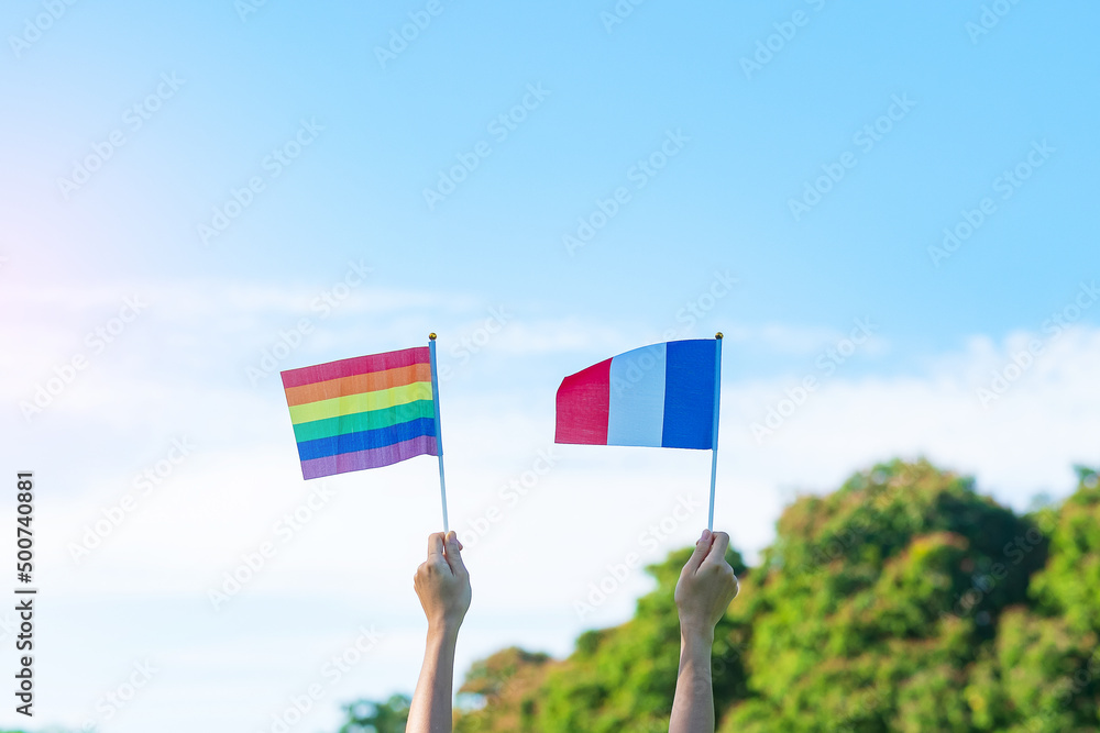 hands showing LGBTQ Rainbow and France flag on nature background. Support Lesbian, Gay, Bisexual, Transgender and Queer community and Pride month concept