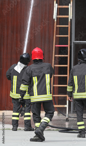 firefighters in action with fire hydrant and ladder in the background during training in the fire station