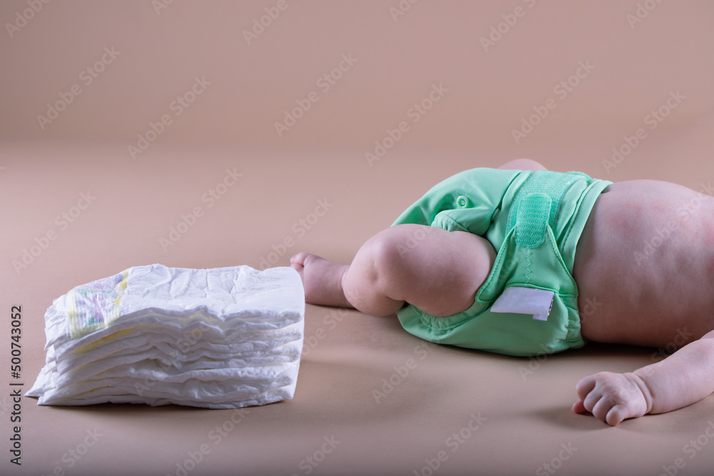 A baby in a diaper at the age of two months and a stack of diapers. How