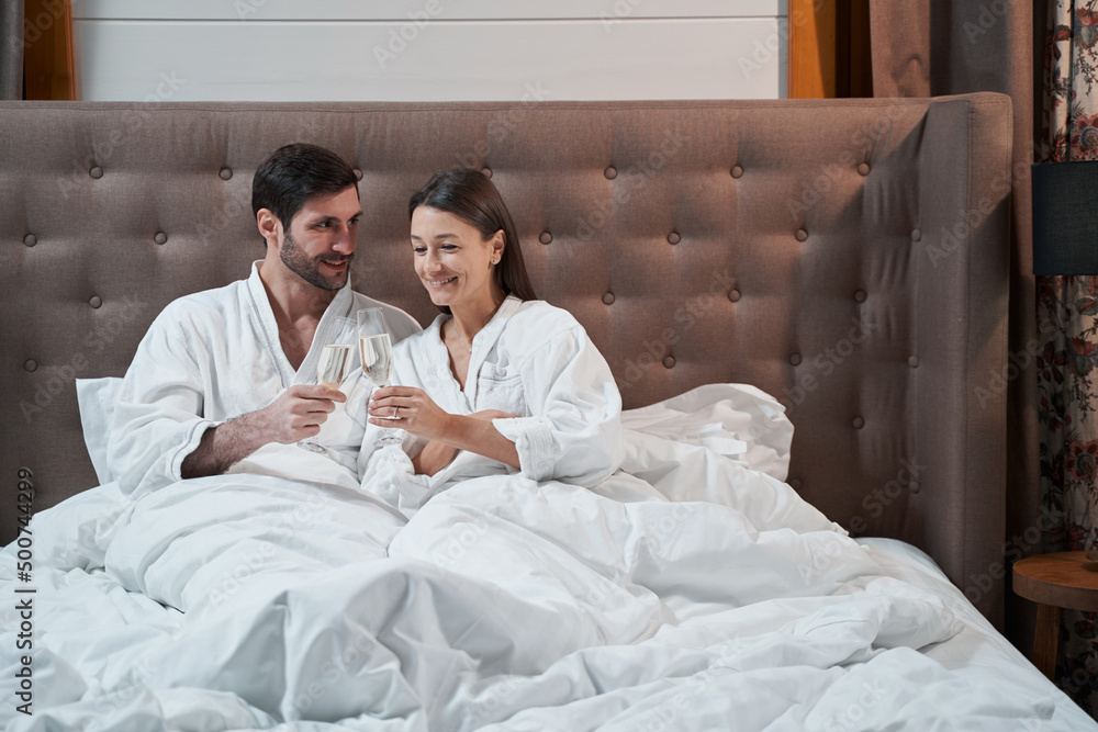 Fototapeta premium Couple clinking their glasses in bed of hotel