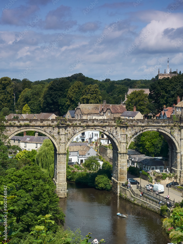 Knaresborough’s viaduct and the River Nidd in bright sunshine and under a blue sky strewn with fluffy cotton-wool clouds.