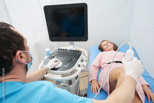 Specialist doctor carefully examining woman knee joint with the help of ultrasound