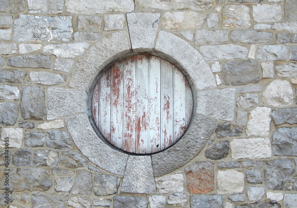 Petite fenêtre ronde nichée sous le toit d'une habitation traditionnelle en pierre, avec volet en bois fermé Petite fenêtre ronde nichée sous le toit d'une habitation traditionnelle en pierre, avec volet en bois fermé