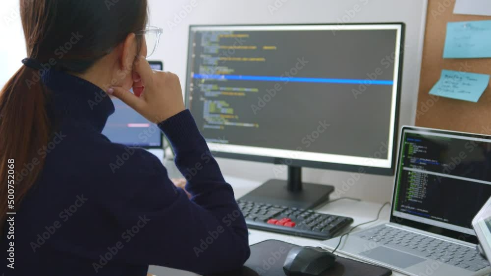Young Asian woman, developer programmer, software engineer, IT support, wearing glasses working on computer to check coding in bugging system. Back view Young Asian woman, developer programmer, software engineer, IT support, wearing glasses working on computer to check coding in bugging system. Back view