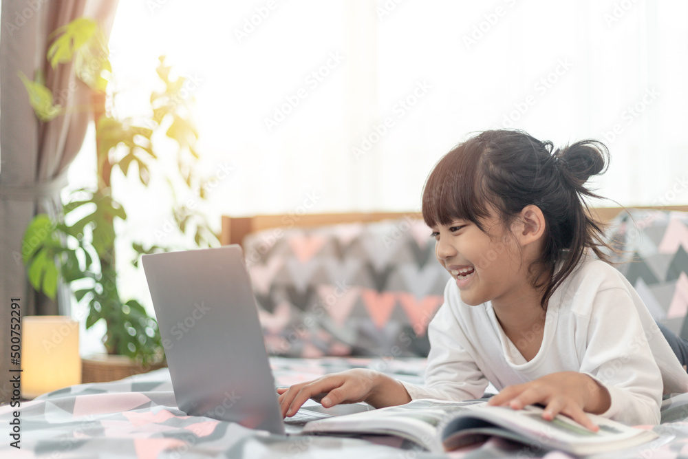 Little Asian girl using a laptop while lying on the bed Little Asian girl using a laptop while lying on the bed