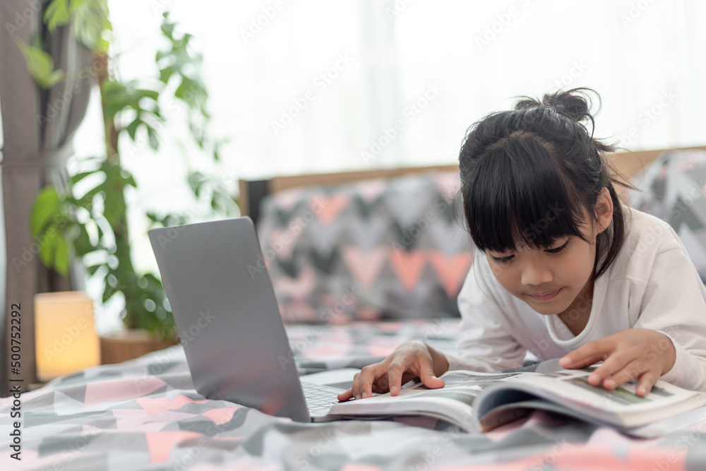 Little Asian girl using a laptop while lying on the bed Little Asian girl using a laptop while lying on the bed