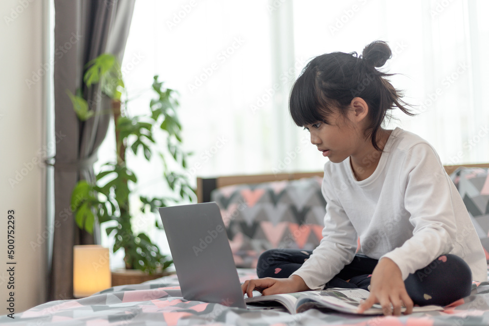 Little Asian girl using a laptop while lying on the bed Little Asian girl using a laptop while lying on the bed