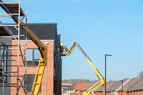 Builders working off Telescopic Boom Lift while fitting insulated sandwich panels to the facade of a new multistorey residential building. Working at height safely photo