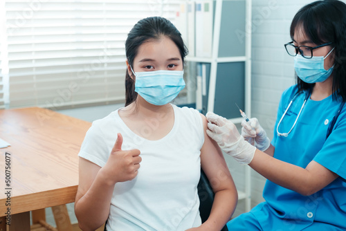 Asian Chinese patient thumbs up happy positive getting vaccinated from covid 19 coronavirus disease pandemic, vaccination with nurse doctor giving needle injection into arm. Wearing surgical facemask