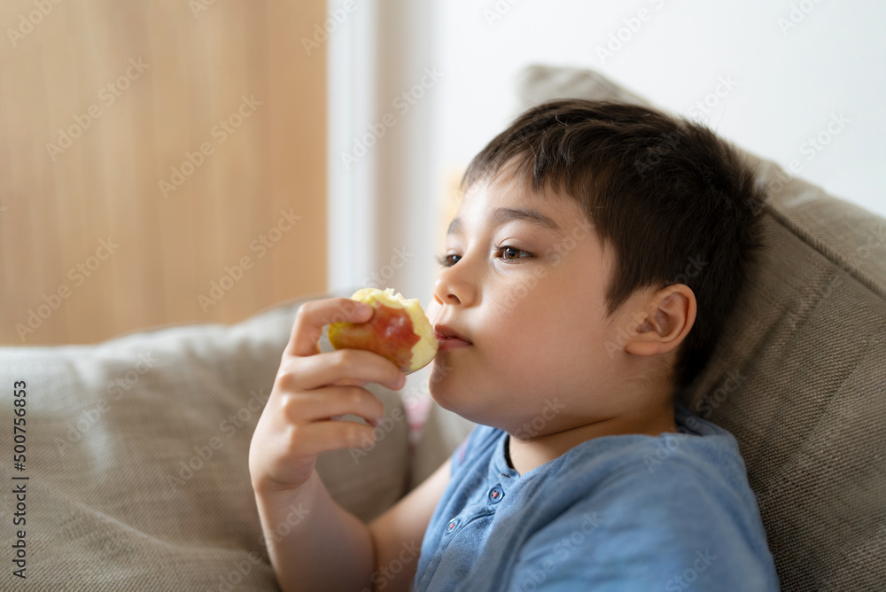 Healthy child eating red apple, Cute boy eating fresh fruit for his snack while watching TV in living room, Close up kid face eating food. Healthy food for children concept Healthy child eating red apple, Cute boy eating fresh fruit for his snack while watching TV in living room, Close up kid face eating food. Healthy food for children concept