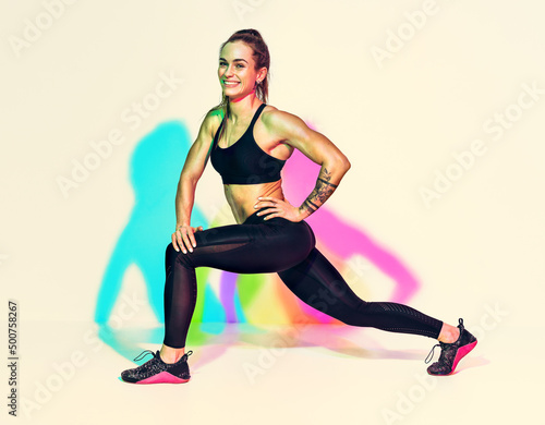 Warming up before training. Photo of laughing woman in black sportswear on white background with effect of rgb colors shadows. Sports motivation and healthy lifestyle