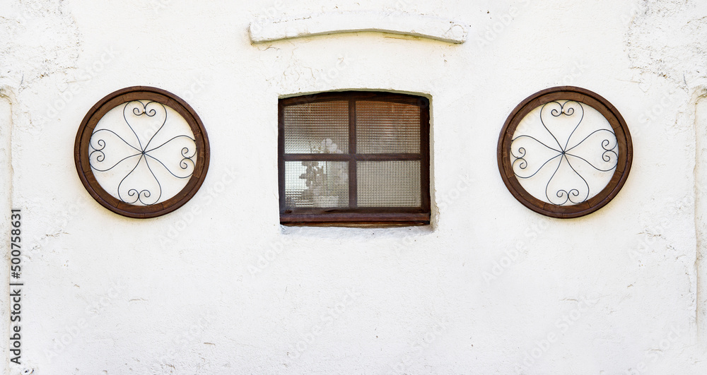 A brown wooden window of an old house, with cottage decoration on the white washed wall - old wall of cottage house - obrazy, fototapety, plakaty 