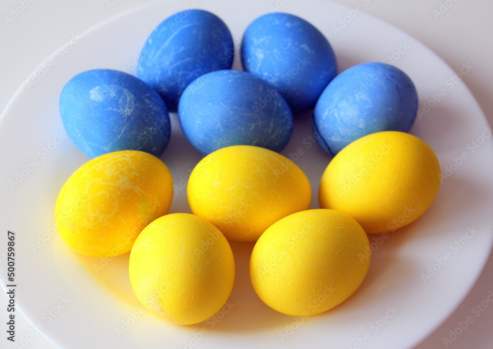 Happy Easter. Horizontal poster with cute painted yellow and blue eggs on a white plate. View from above. Happy Easter. Horizontal poster with cute painted yellow and blue eggs on a white plate. View from above.