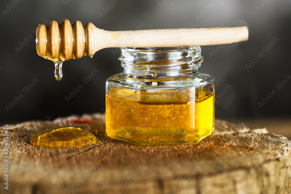Honey jar and dripper on tree stump. grey background. Honey jar and dripper on tree stump. grey background.