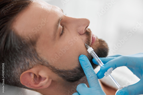Mature person with beard undergoes nasolabial fold filler procedure with skilled beautician in salon photo