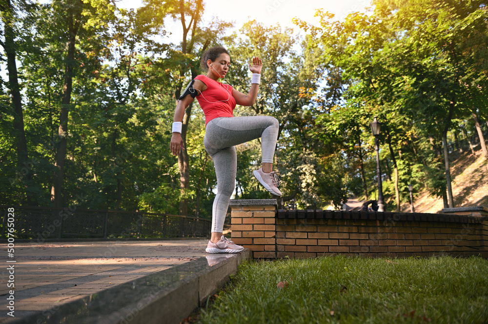 Full length portrait of a charming active woman in tight sportswear exercising outdoors doing leg muscle exercises on the steps of a forest park on a summer day. Fitness, sport, healthy lifestyle