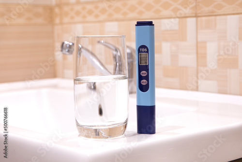 Measurement of TDS of water. Electronic pH meter in a glass of water. In the background is a tap for drinking water. Cleaning the water in the bathroom. photo