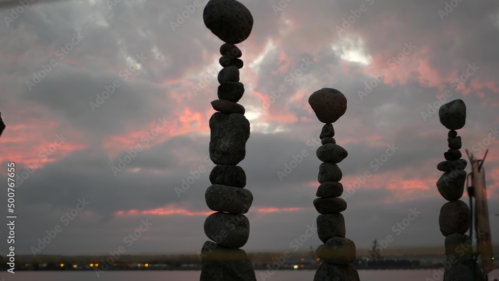 Rock balancing against cloudy dramatic sky on sunset. Stack of stones in balance, stable pyramid in pink twilight of evening. Cloudscape at sundown time by sea ocean water. Buddhism concept.