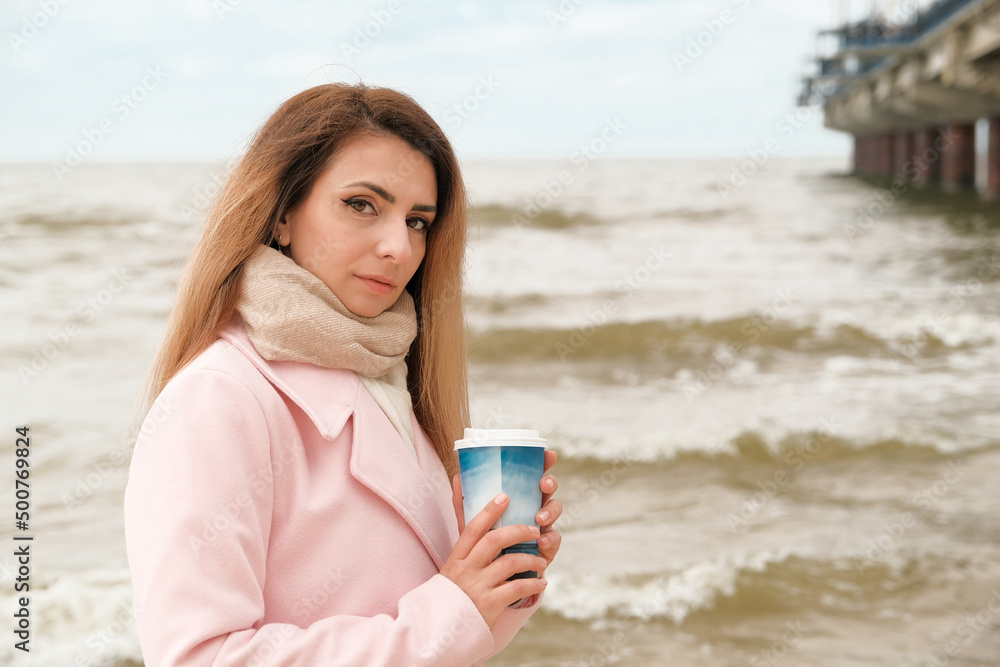 a beautiful girl of Italian appearance drinks coffee on the embankment. girl in a pink coat