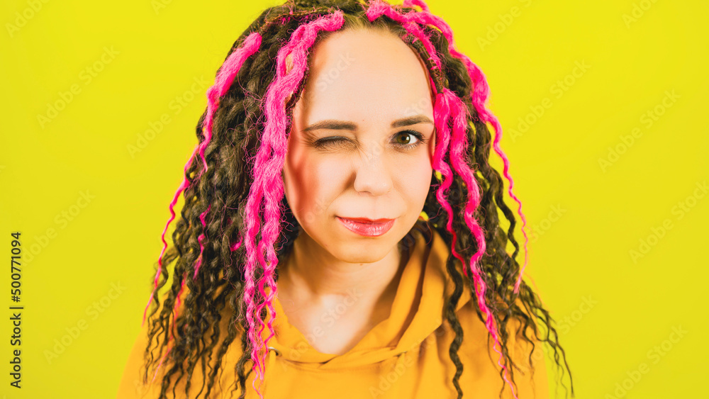 Young beautiful woman with curly hairstyle smiling and winking on yellow background. Positive female with dreadlocks looking at camera and flirting. Young beautiful woman with curly hairstyle smiling and winking on yellow background. Positive female with dreadlocks looking at camera and flirting.