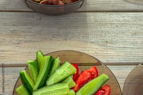 Background from a wooden table on which there are a plate with cucumbers and tomatoes and a bowl of meat kebab.