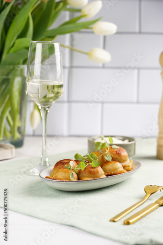 Deep fried traditional italian dish - ravioli, dumplings stuffed with minced meat, oregano branch, sour cream, a glass with champagne on green table cloth