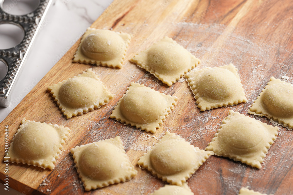 Freshly made traditional italian dish - ravioli, dumplings stuffed with minced meat, on wooden board with flour, aluminum form for preparation