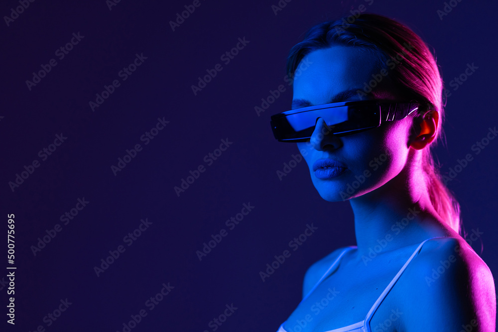 Young woman posing in a studio in a trendy neon light. Woman in sunglasses and hoodie with colorful light effects. Young woman posing in a studio in a trendy neon light. Woman in sunglasses and hoodie with colorful light effects.