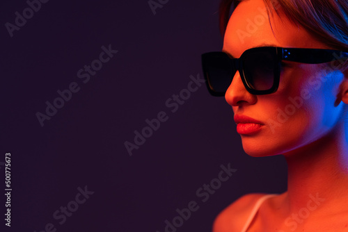 young woman adjusting sunglasses and posing isolated on purple