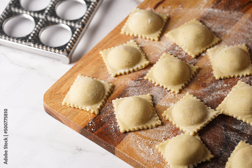 Freshly made traditional italian dish - ravioli, dumplings stuffed with minced meat, on wooden board with flour, aluminum form for preparation