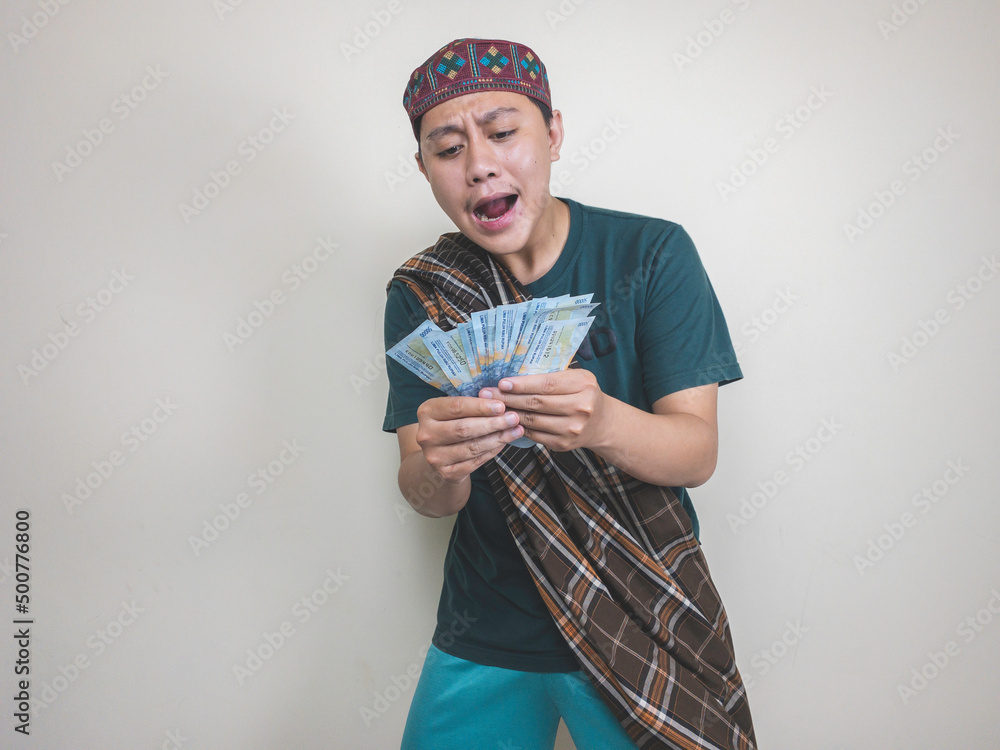 Happy asian man while holding a indonesian money. Isolated on white. Ramadan concept Happy asian man while holding a indonesian money. Isolated on white. Ramadan concept