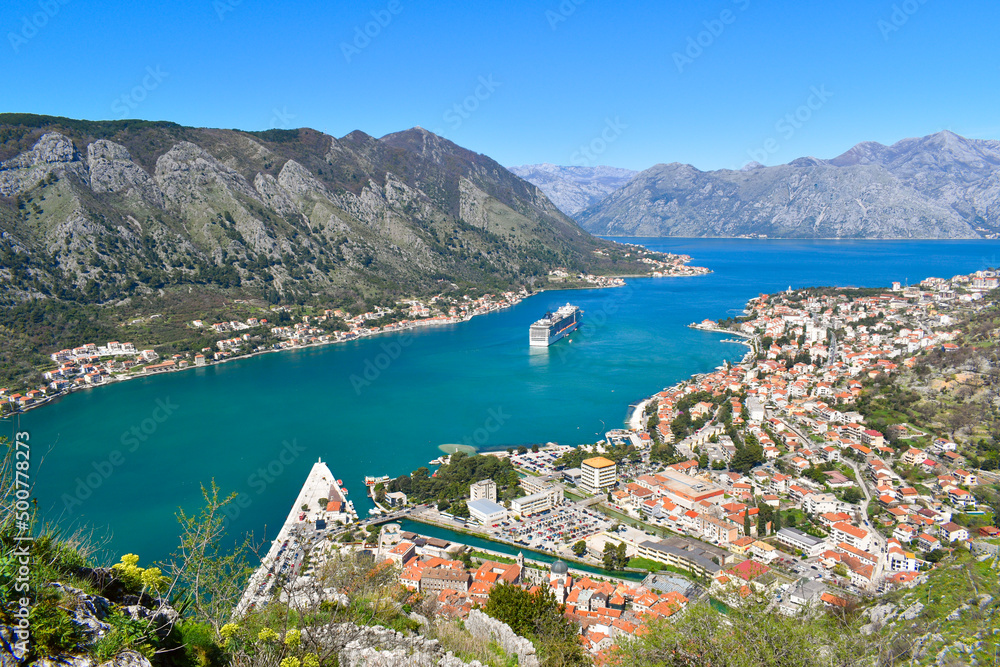 Kotor, Montenegro, Europe. Bay of Kotor on Adriatic Sea. Roofs of the buildings in the old town. Cruise in the bay, mountains in the background. Clear blue sky, sunny day
