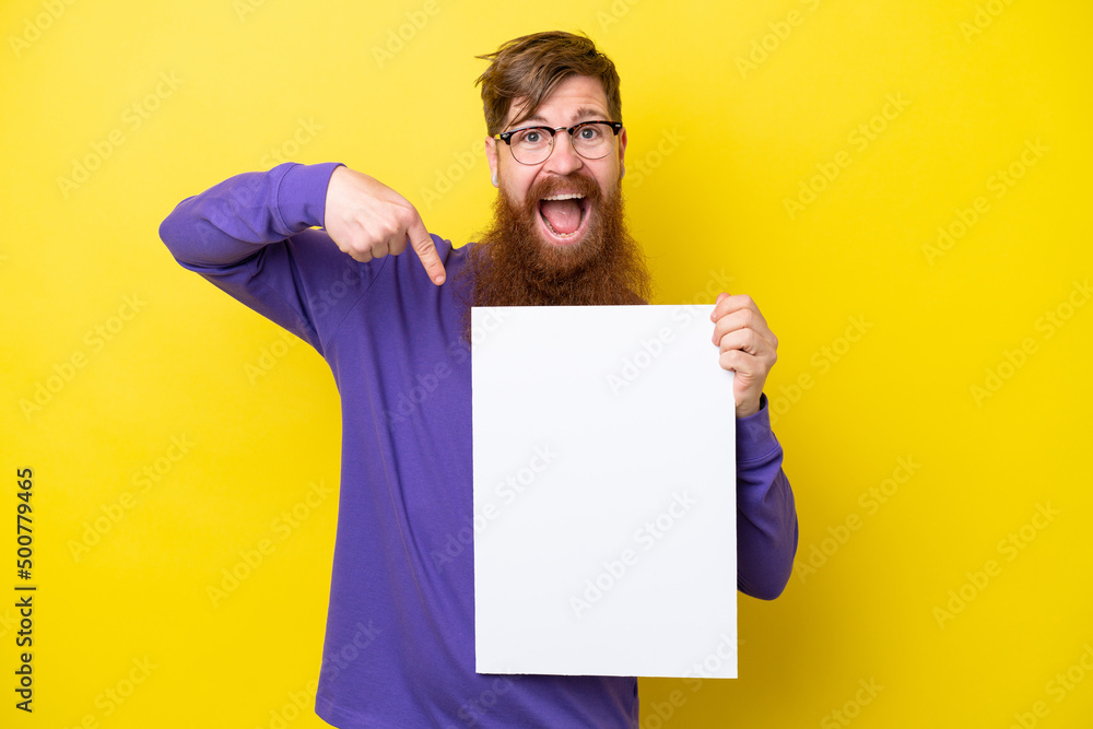 Redhead man with beard isolated on yellow background holding an empty placard with happy expression and pointing it Redhead man with beard isolated on yellow background holding an empty placard with happy expression and pointing it