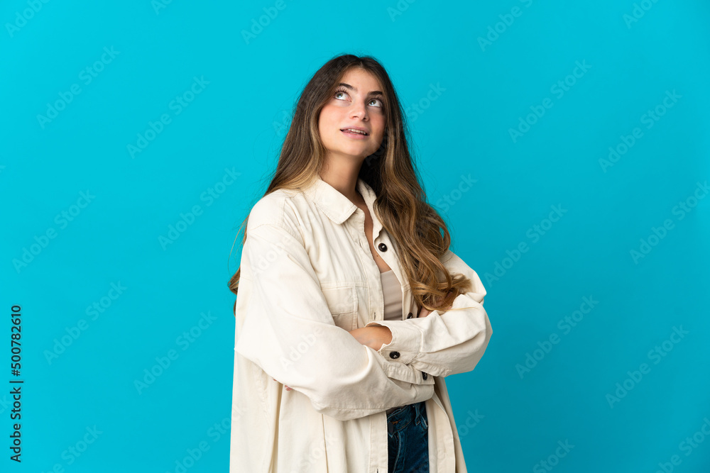 Young caucasian woman isolated on blue background looking up while smiling Young caucasian woman isolated on blue background looking up while smiling